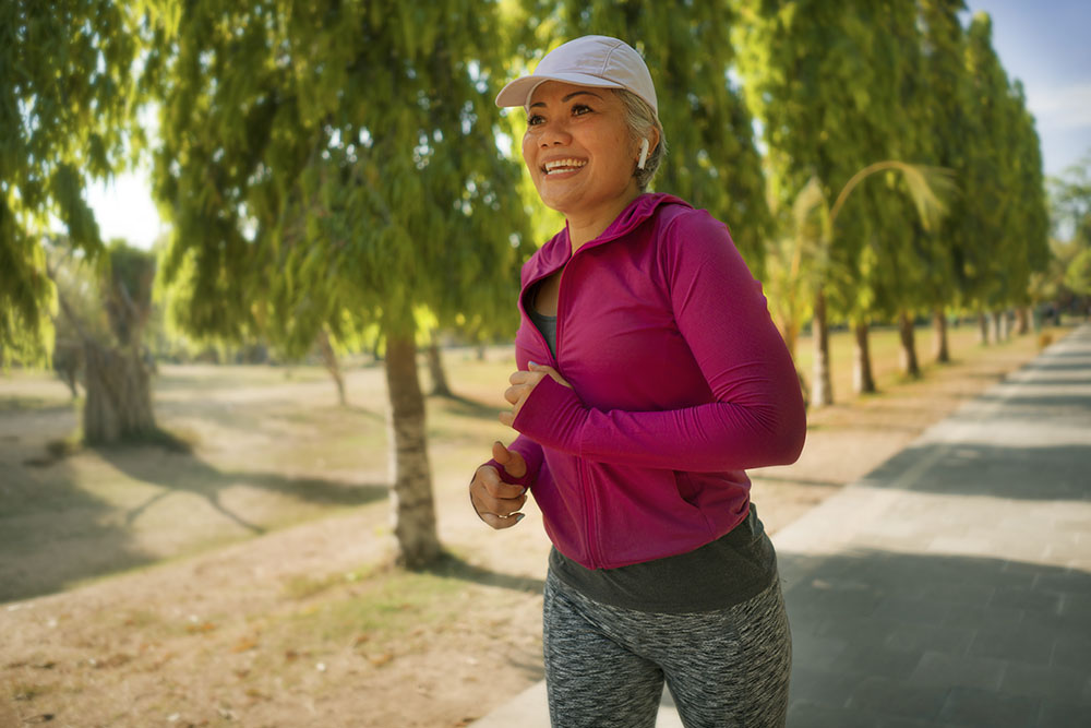 attractive middle aged lady running happy at city park . beautiful and sporty woman on her 40s exercising doing jogging workout on a sunny morning enjoying healthy lifestyle and fitness